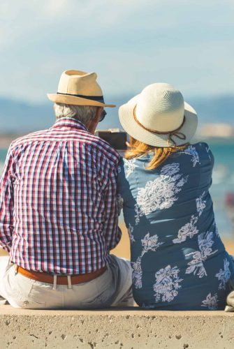 Loving the elderly couple sitting on the wall facing the beach, watching and taking pictures of the landscape on a romantic trip